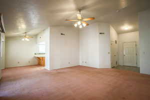 Carpeted empty room featuring ceiling fan and a high textured ceiling