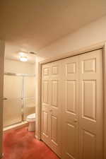 Full bath with a closet, a shower stall, carpet flooring, and a textured ceiling