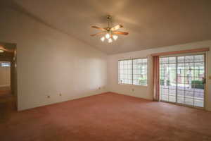 Carpeted empty room with vaulted ceiling, plenty of natural light, and a ceiling fan