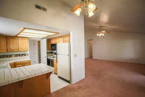 Kitchen featuring tile countertops, white appliances, light carpet, ceiling fan, and a peninsula