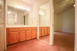 Full bath with vanity, light carpet, ceiling fan, and vaulted ceiling