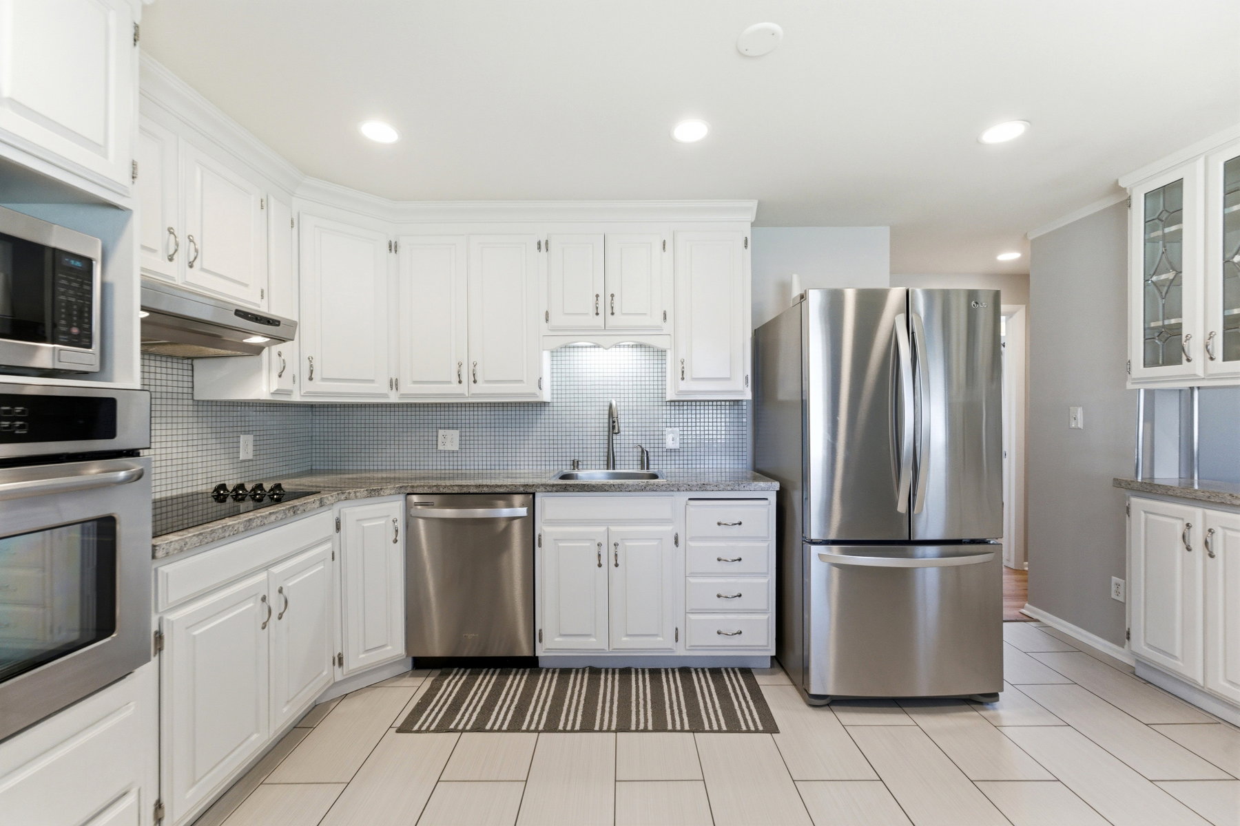 Kitchen with stainless steel appliances, white cabinets, recessed lighting, glass insert cabinets, and tasteful backsplash