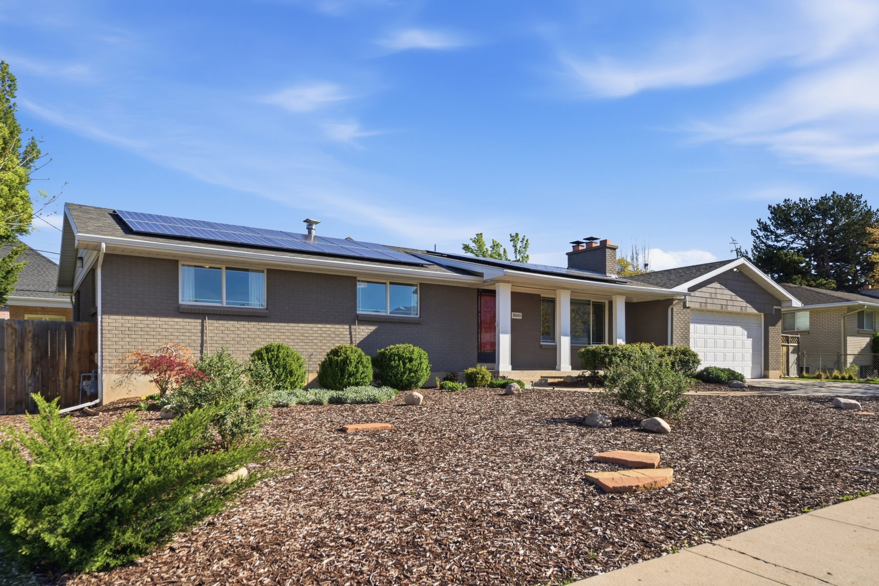 Ranch-style home with roof mounted solar panels, an attached garage, a porch, a chimney, and brick siding