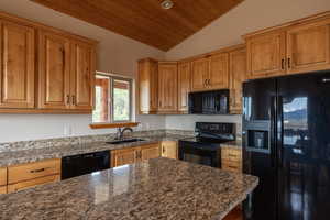 Kitchen with black appliances, a vaulted wooden ceiling, dark stone countertops, and wood finish cabinetry