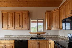 Kitchen with black appliances, dark stone countertops, and wood finish cabinetry