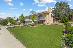 View of front of house featuring a chimney, brick siding, and a balcony