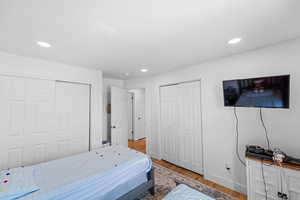 Bedroom with two closets, light wood-type flooring, and recessed lighting