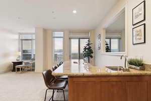 Indoor wet bar with light colored carpet, light stone countertops, recessed lighting, and wood finish cabinets