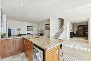 Kitchen with a peninsula, open floor plan, wine cooler, light stone counters, and wood finish cabinetry