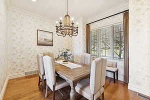 Dining area with wallpapered walls, suspended lighting, crown molding, and light wood-style flooring
