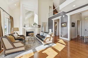 Living area with light wood finished floors, a tiled fireplace, a high ceiling, and recessed lighting