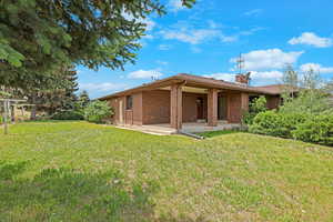 Back of house with a patio area, brick siding, a lawn, and a chimney