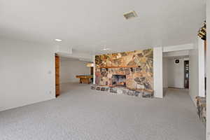 Unfurnished living room featuring carpet, a textured ceiling, and a stone fireplace