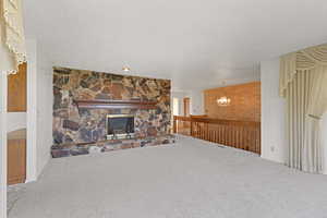 Unfurnished living room featuring a textured ceiling, carpet, a chandelier, and a stone fireplace