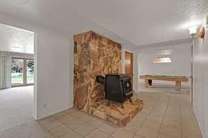 Carpeted living area featuring a textured ceiling, tile patterned floors, a wood stove, and billiards table