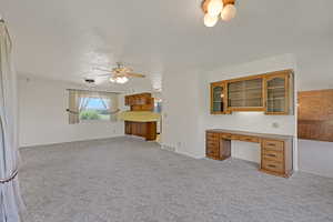 Unfurnished living room featuring light carpet, a ceiling fan, a textured ceiling, and an office area