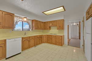 Kitchen featuring white appliances, light countertops, light floors, brown cabinetry, and a textured ceiling