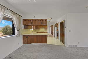 Kitchen featuring light carpet, a peninsula, light countertops, stainless steel oven, and a textured ceiling