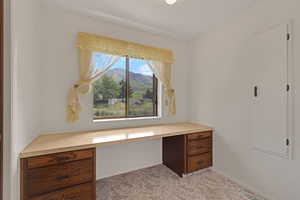 Unfurnished office featuring built in study area, light carpet, and a mountain view