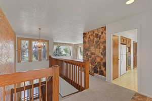Corridor featuring a chandelier, an upstairs landing, and a textured ceiling