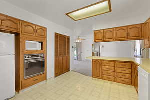 Kitchen featuring white appliances, light countertops, brown cabinets, a peninsula, and a textured ceiling