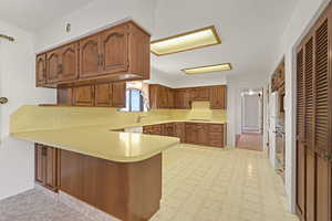 Kitchen with a peninsula, a textured ceiling, light countertops, stovetop, and brown cabinetry