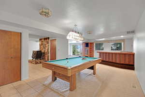 Recreation room featuring a wood stove, a textured ceiling, light tile patterned floors, and billiards