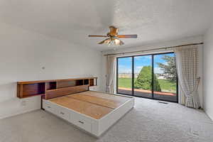 Unfurnished bedroom featuring access to outside, light colored carpet, a textured ceiling, and ceiling fan