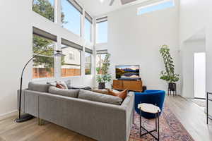 Living room with light wood-style floors, plenty of natural light, a high ceiling, and ceiling fan