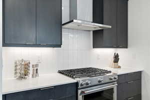 Kitchen with stainless steel range, modern cabinets, backsplash, light stone counters, and dark cabinetry