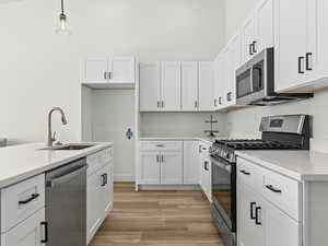 Kitchen with stainless steel appliances, light wood-type flooring, white cabinetry, hanging light fixtures, and light stone countertops