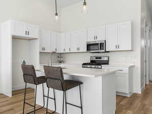 Kitchen featuring a high ceiling, a breakfast bar area, an island with sink, stainless steel appliances, and white cabinets