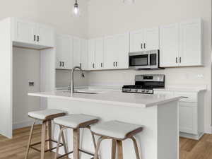 Kitchen with white cabinets, a breakfast bar area, stainless steel appliances, and light wood-style flooring