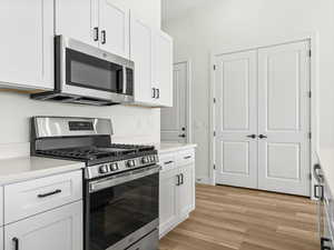 Kitchen featuring stainless steel appliances, white cabinetry, light wood-style floors, and light stone countertops