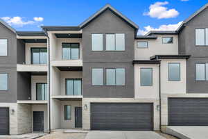 Modern home featuring stucco siding, a balcony, a garage, concrete driveway, and stone siding