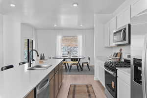 Kitchen with stainless steel appliances, light wood-style flooring, light stone countertops, a kitchen bar, and recessed lighting