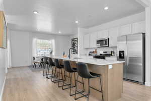Kitchen with an island with sink, stainless steel appliances, a kitchen breakfast bar, light wood finished floors, and light stone countertops