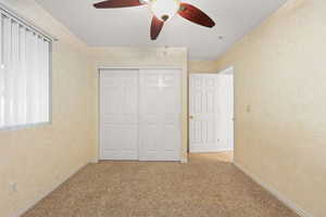 Same Spare bedroom with ceiling fan, light carpet, and a closet at another angle.
