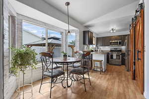 Dining room with a sliding barn door to the pantry, light wood-style floors, and lofted ceiling