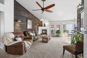 Carpeted living room featuring vaulted ceiling, a fireplace, ceiling fan, and an accent wall