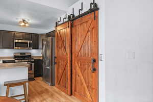Kitchen with a sliding barn door to the pantry, stainless steel appliances, light countertops, light wood-type flooring, and dark wood finish cabinetry