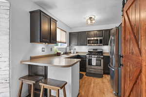 Kitchen featuring a barn sliding door to the pantry, stainless steel appliances, a kitchen bar, a peninsula, and light wood finished floors