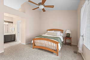 Bedroom with light colored carpet, lofted ceiling, on suit bathroom, ceiling fan, and multiple windows