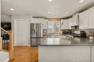 Kitchen with stainless steel appliances, a peninsula, white cabinets, dark  counters, and light wood-style floors