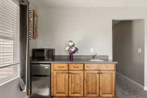 Bar area featuring freestanding refrigerator, black microwave, dark countertops, and wood finish cabinets
