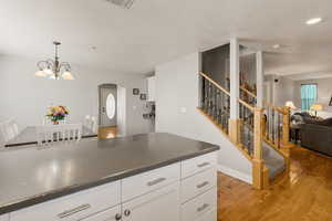 Kitchen featuring white cabinetry, open floor plan, light wood-type flooring, hanging lights, and arched walkways