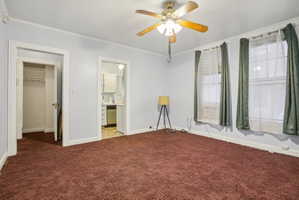Unfurnished bedroom featuring a walk in closet, ornamental molding, carpet floors, ceiling fan, and connected bathroom