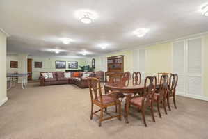 Dining space with light colored carpet, crown molding, and a textured ceiling