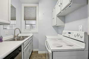 Kitchen featuring white range with electric cooktop, light countertops, white cabinets, stainless steel dishwasher, and stone finish floors