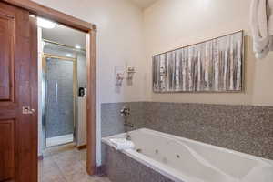 Bathroom with a stall shower, light tile patterned flooring, and a whirlpool tub